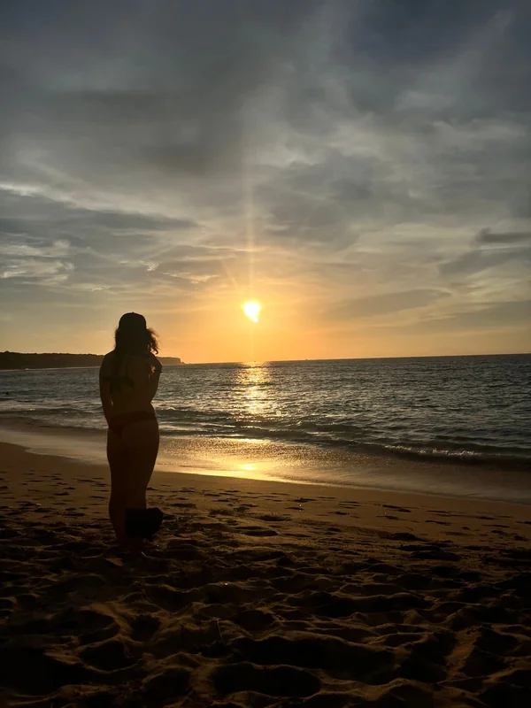 Silueta de mujer contemplando el sol cayendo sobre el océano índico en una playa del sur de Bali