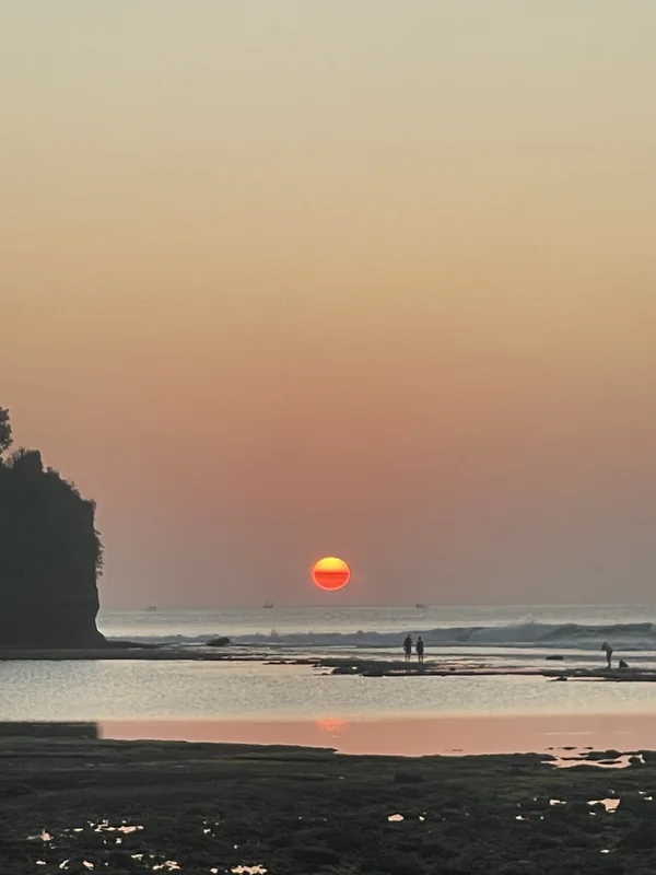 Sol naranja descendiendo sobre el mar con surfistas en silueta en una playa cerca de Uluwatu, Bali