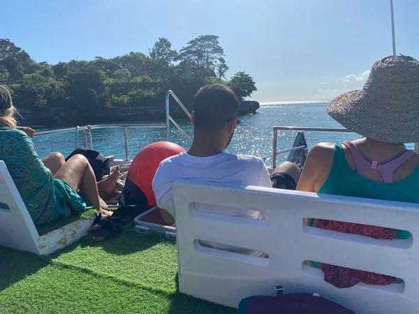 Grupo de viajeros relajados en cubierta de una lancha rápida bordeando los acantilados verdes de Nusa Penida