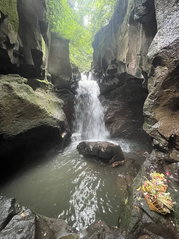 Cascada cayendo entre paredes de roca con ofrendas balinesas en la base, cañón de Tukad Cepung, Bali