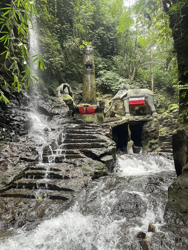 Cascada sagrada con escalones de piedra, estatua de elefante tallado y altar balinés en templo de Sebatu