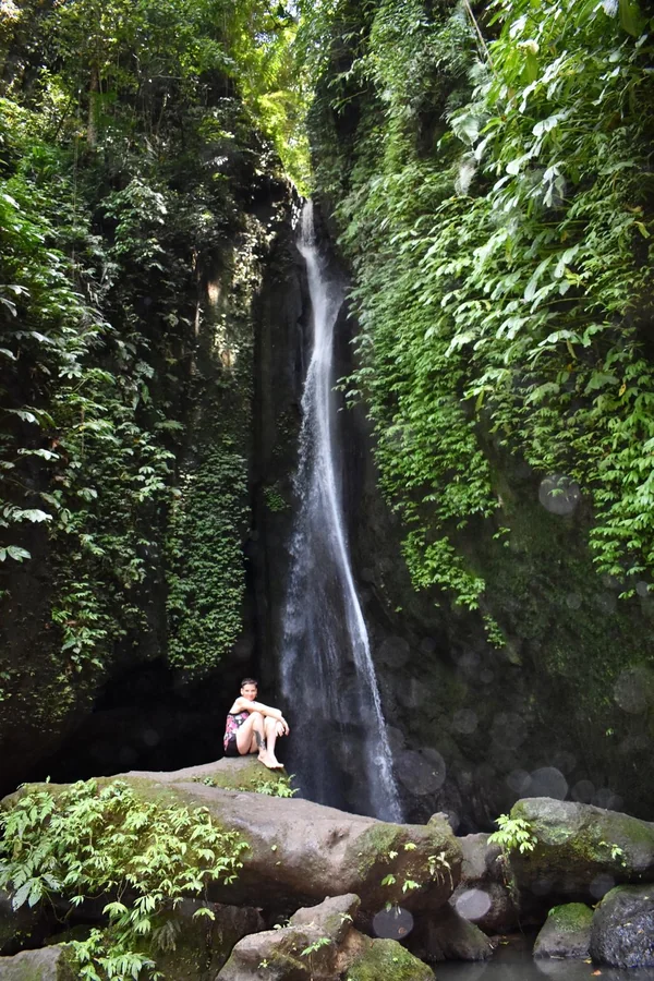 Chorro fino de agua cayendo por un acantilado verde cubierto de vegetación tropical en una cascada escondida cerca de Ubud