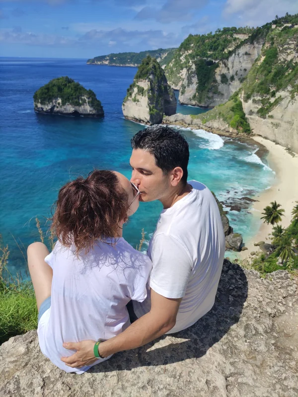 Pareja besándose sentada en el mirador con vista a las playas blancas e islotes de Diamond Beach en Nusa Penida