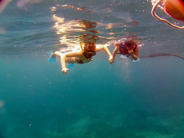 Dos niñas haciendo snorkel agarradas de la mano sobre las aguas cristalinas de Nusa Penida, tour familiar en Bali