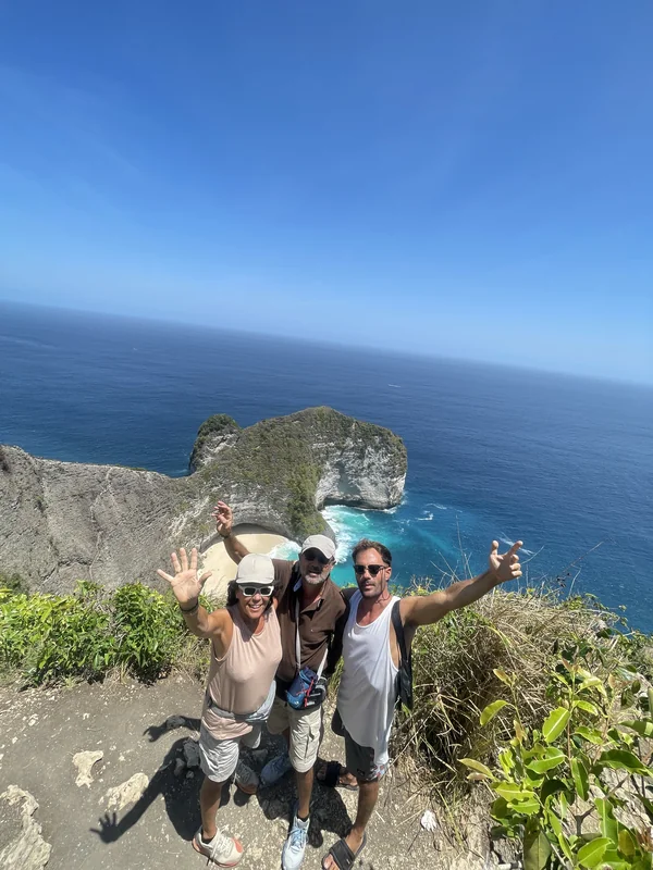 Grupo de tres viajeros felices con los brazos en alto en el mirador de Kelingking Beach, Nusa Penida