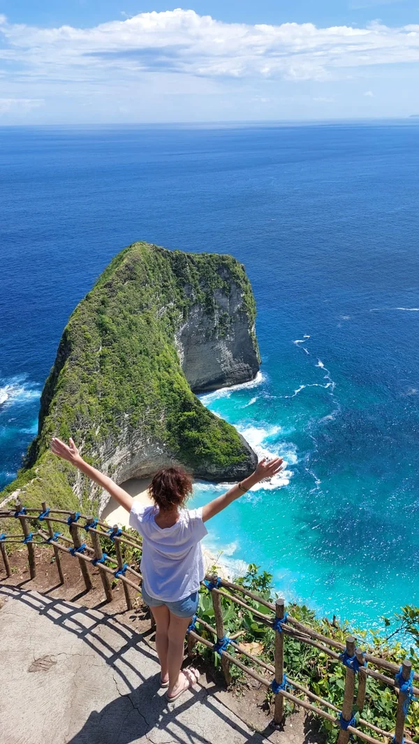 Mujer con los brazos abiertos en el mirador vertical de Kelingking Beach contemplando la forma de t-rex del acantilado en Nusa Penida
