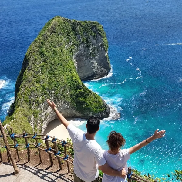 Pareja abrazada con los brazos abiertos en el mirador del acantilado en forma de tiranosaurio de Kelingking Beach, Nusa Penida