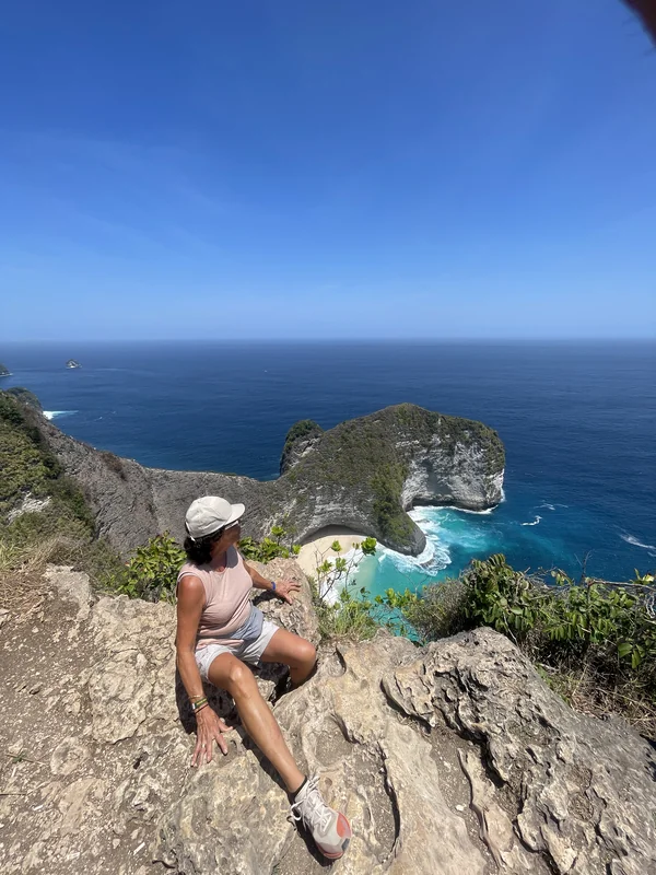 Mujer contemplando la vista de Kelingking Beach con los acantilados blancos y aguas cristalinas turquesas de Nusa Penida