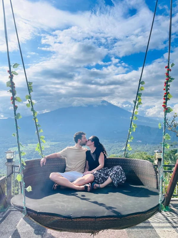 Pareja besándose en el sofá colgante de Lahangan Sweet con el cono perfecto del volcán Monte Agung al fondo