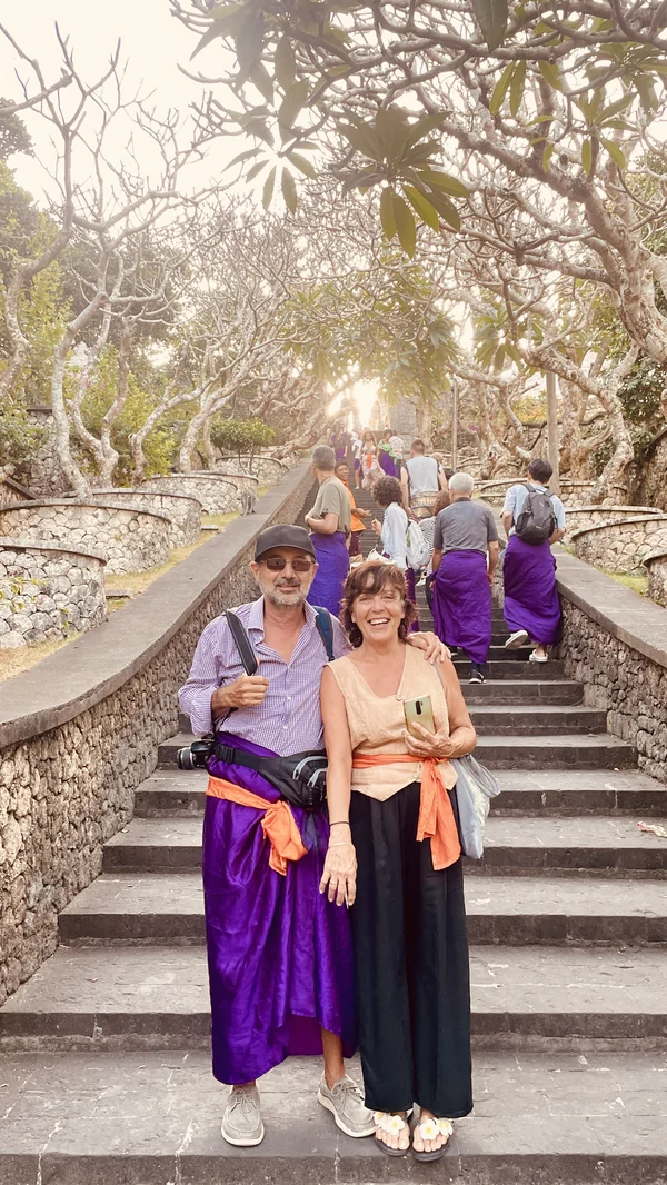 Pareja con sarongs tradicionales en las escaleras del templo de Uluwatu al atardecer entre árboles de frangipani, Bali