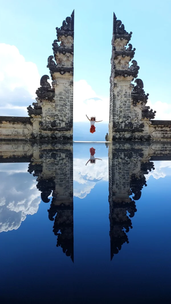 Persona saltando entre las puertas partidas del templo Pura Lempuyang con el efecto reflejo en espejo característico de las puertas del cielo