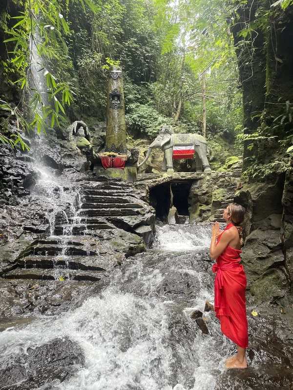 Mujer con sarong rojo realizando ritual de purificación frente a la cascada sagrada de Sebatu, Bali