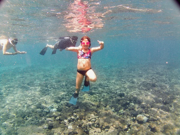 Niña haciendo snorkel con aletas, chaleco y gafas mostrando pulgares arriba sobre arrecife de coral en Nusa Penida, Bali