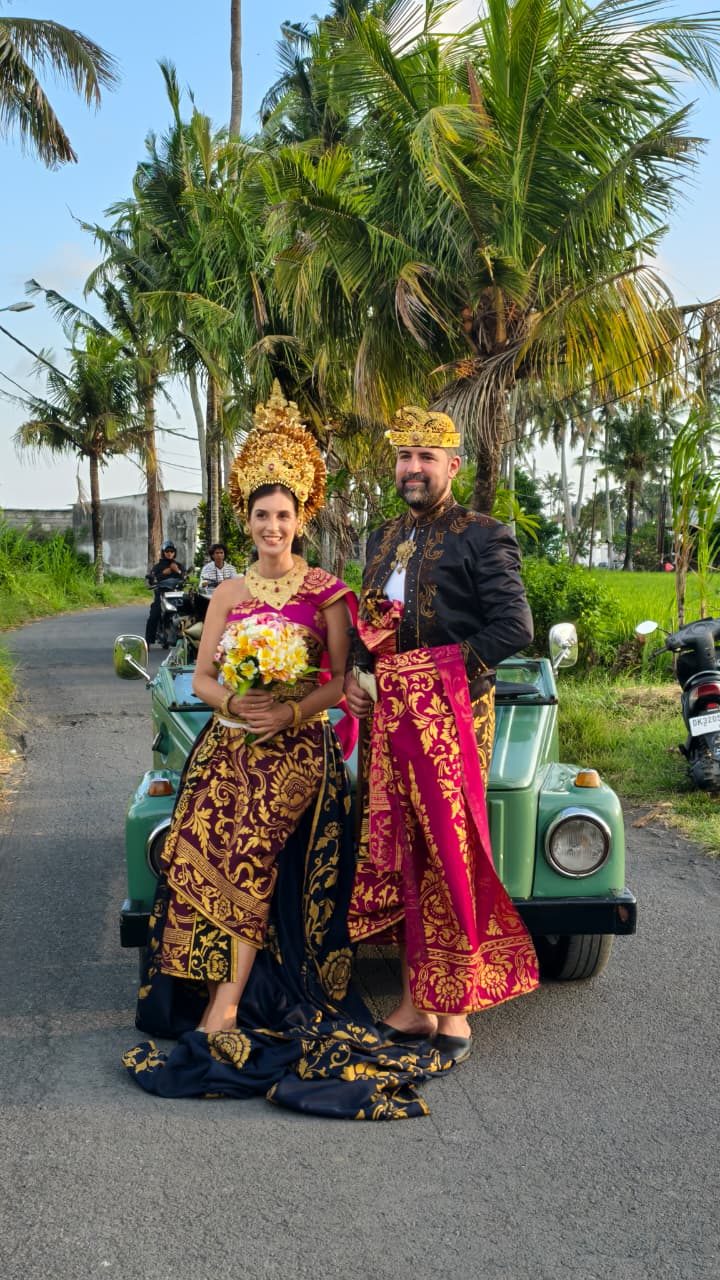 Pareja recién casada con trajes balineses y coche de época verde en Bali