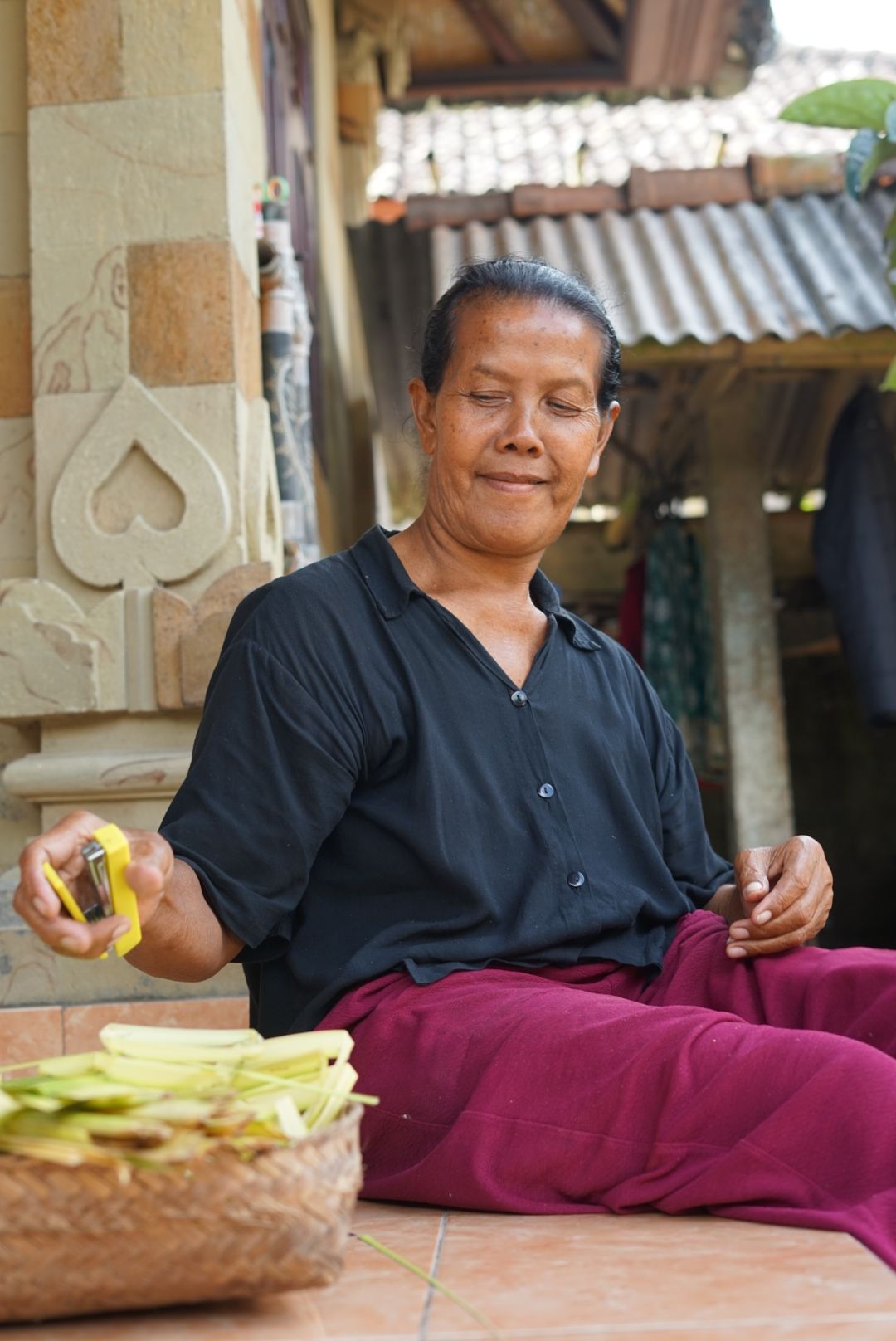 Mujer balinesa preparando ofrendas canang sari cortando tiras de hoja de palma lontar en su casa de Bali