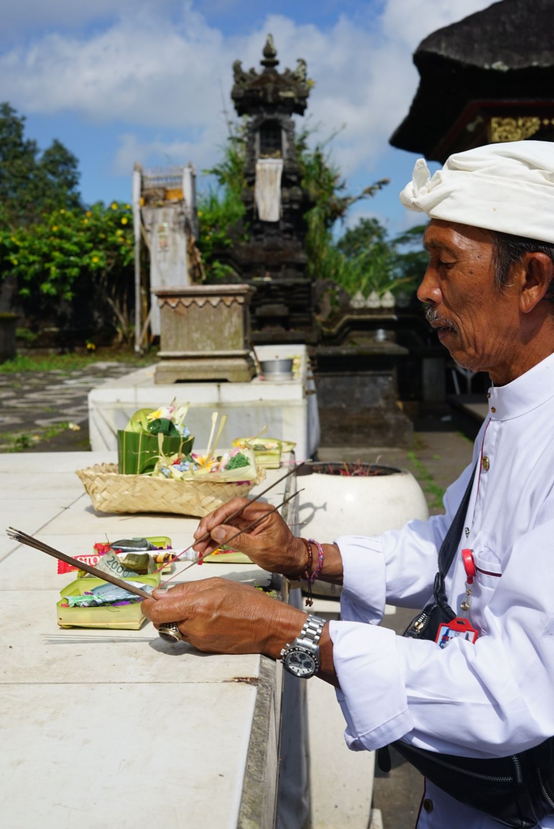 Sacerdote balinés pemangku encendiendo incienso sobre canang sari en altar de templo hindú en Bali