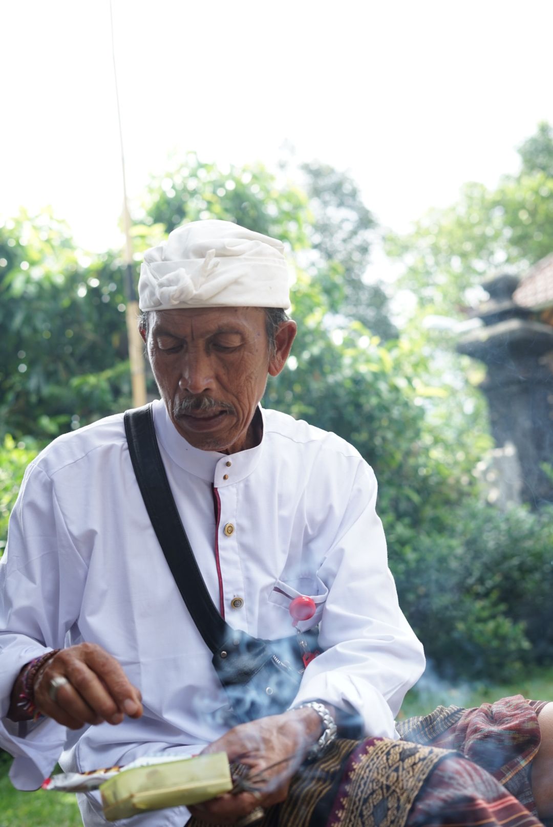 Pemangku balinés sosteniendo canang sari con incienso humeante en una ceremonia tradicional en Bali